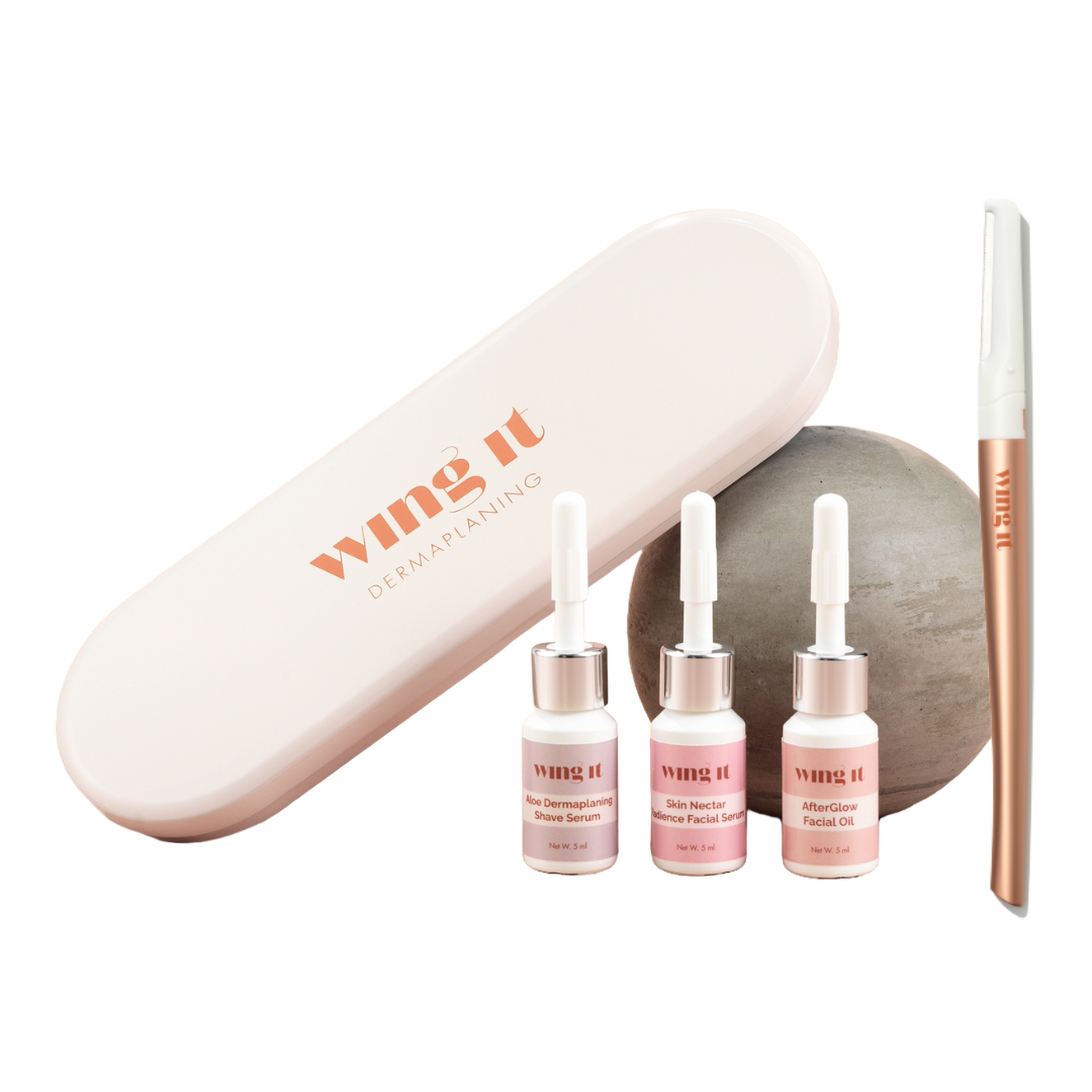 Dermaplaning creme tin next to a sphere and 3 small facial product bottles and a golden wing it dermaplaning razor