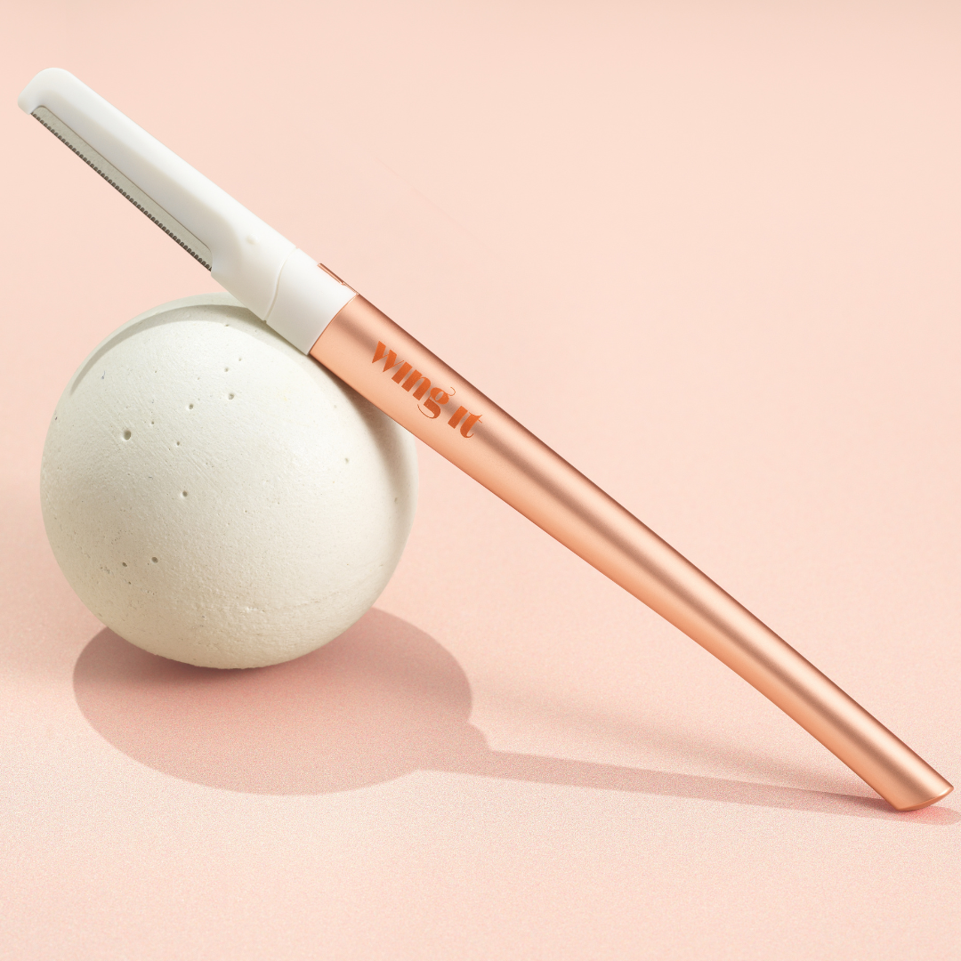 Golden Dermaplaning Razor resting on a stone sphere