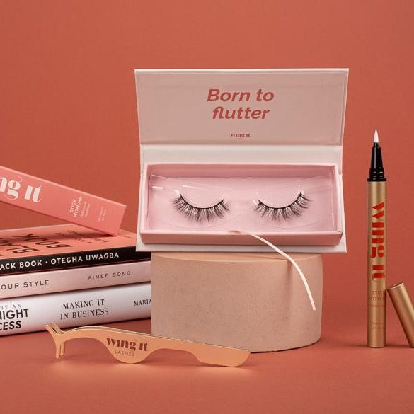 Set with pair of Wing It Cosmetics luxury false eyelashes with adhesive eyeliner with open books.