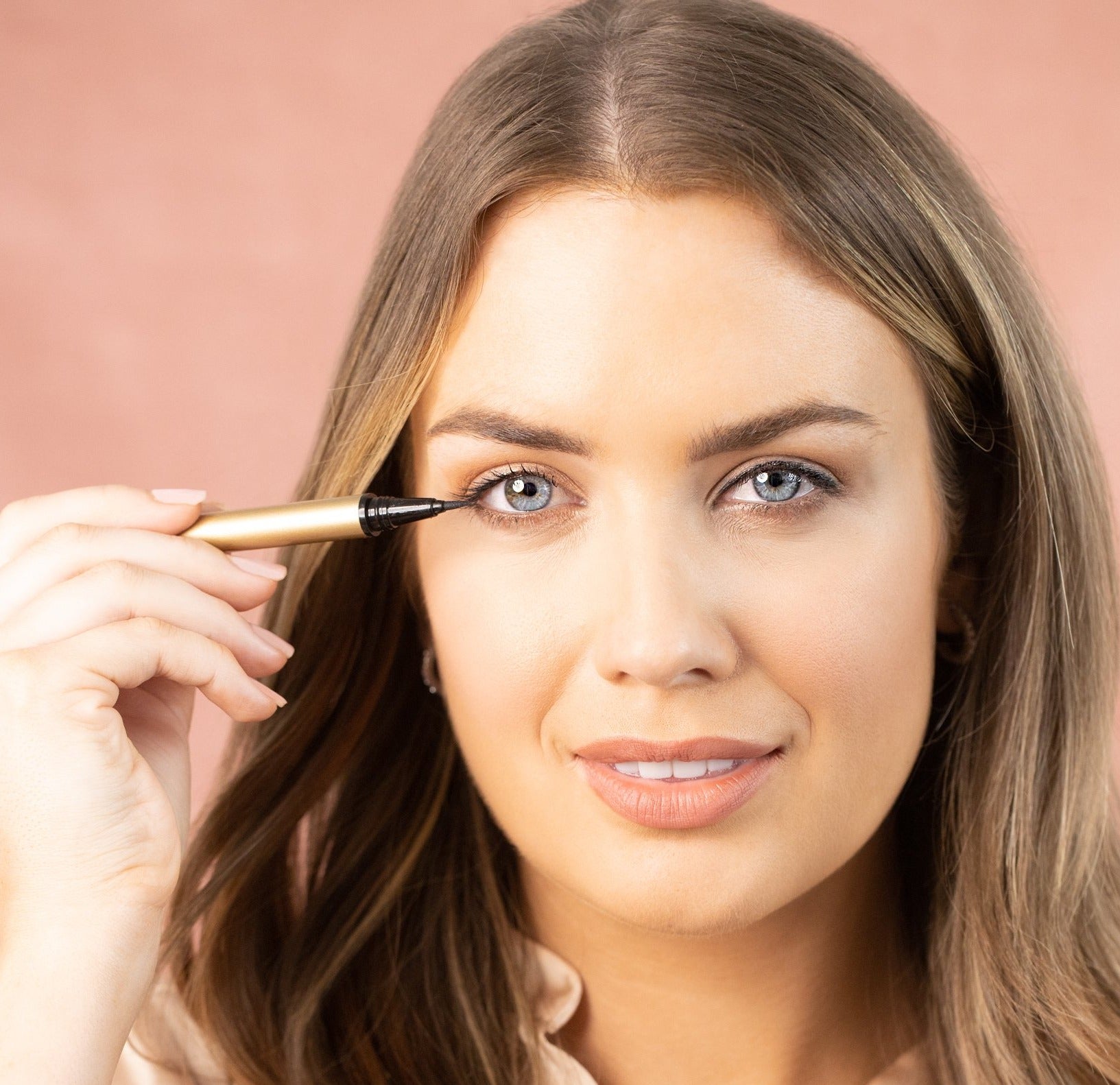 Model applying STICK WITH ME adhesive felt tip black eyeliner. Waterproof, 24 hour hold. Gold tube.