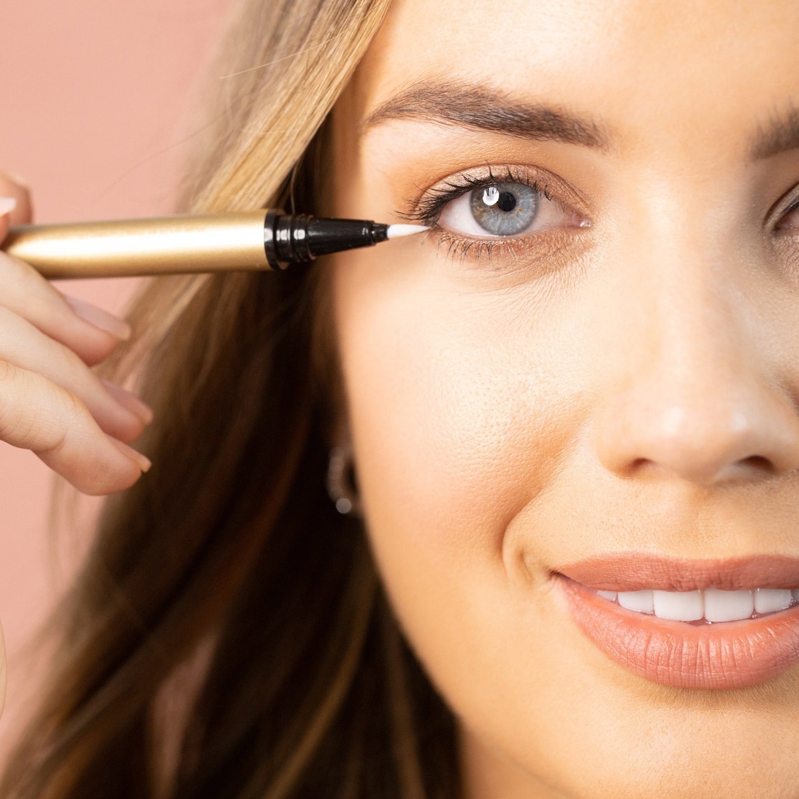 Model applying STICK WITH ME adhesive felt tip clear eyeliner. Waterproof, 24 hour hold. Gold tube.